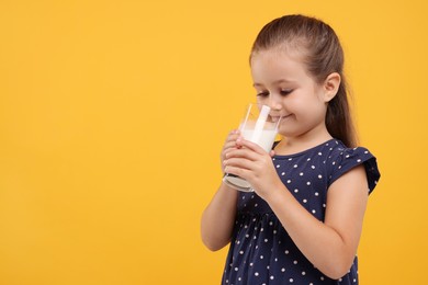 Photo of Cute girl drinking fresh milk from glass on orange background, space for text