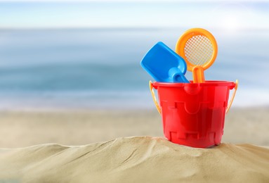 Image of Plastic toy set with shovel on sandy beach near sea, space for text 