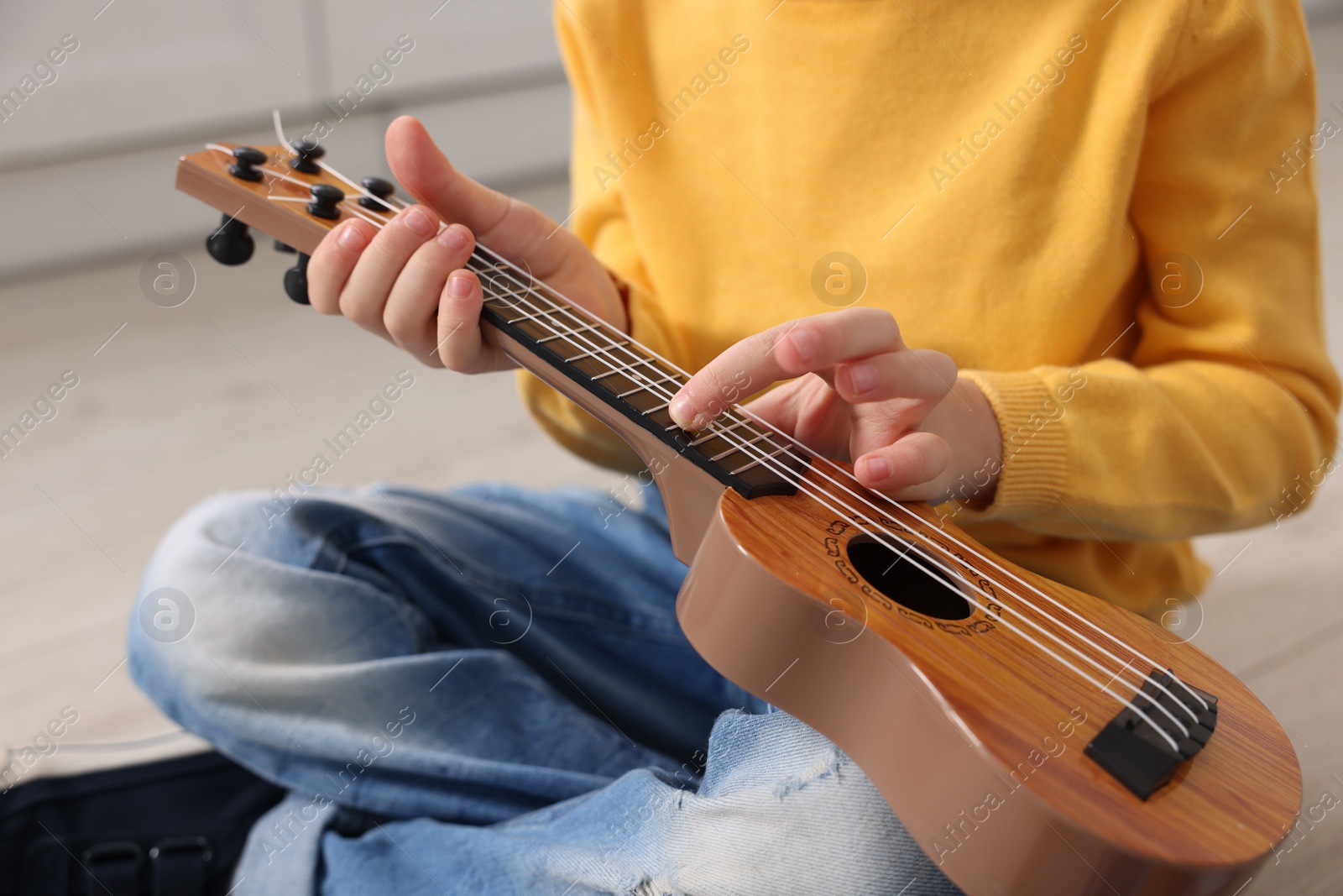 Photo of Little boy playing toy guitar indoors, closeup