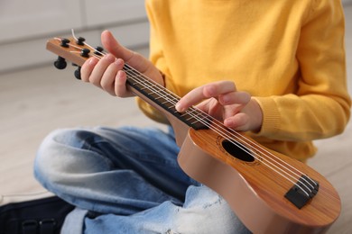 Little boy playing toy guitar indoors, closeup