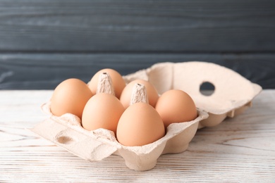 Photo of Carton of raw chicken eggs on wooden table against gray background