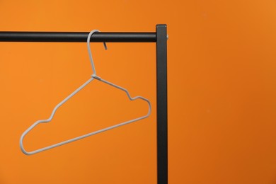 Photo of Empty clothes hanger on rack against orange background. Space for text