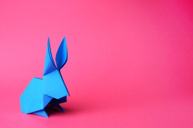Photo of Light blue paper bunny on pink background, space for text. Origami art