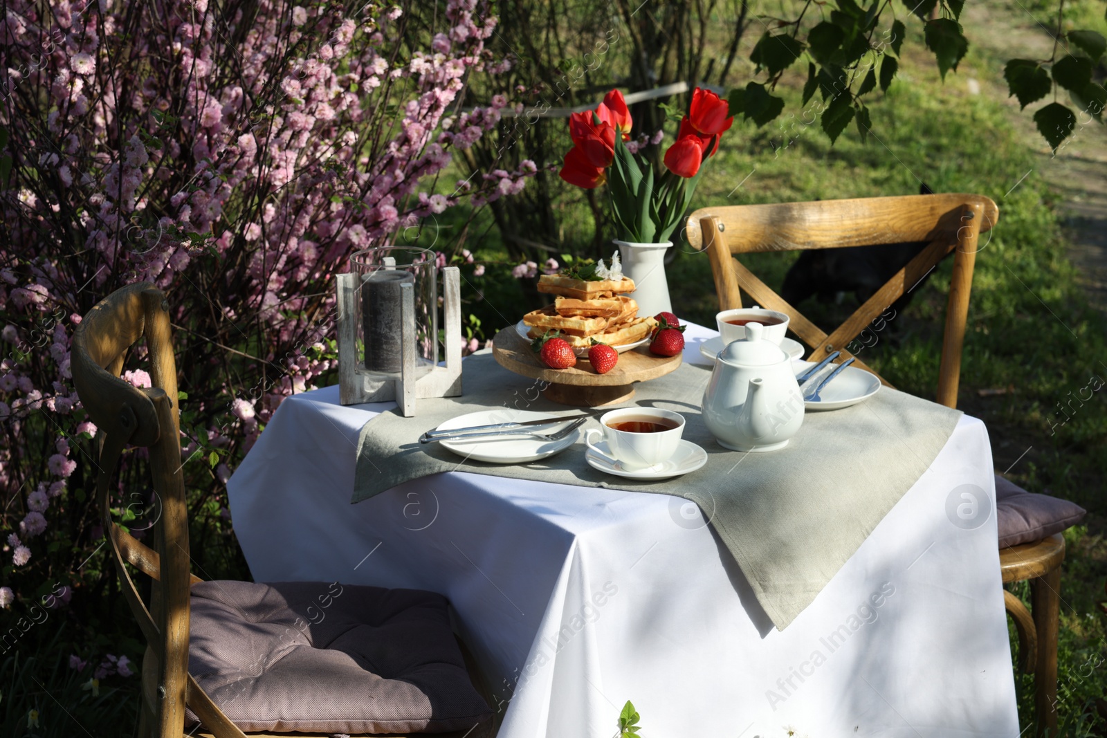 Photo of Beautiful bouquet of tulips and freshly baked waffles on table served for tea drinking in garden