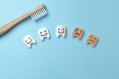 Clean and dirty decorative teeth near toothbrush on light blue background, flat lay