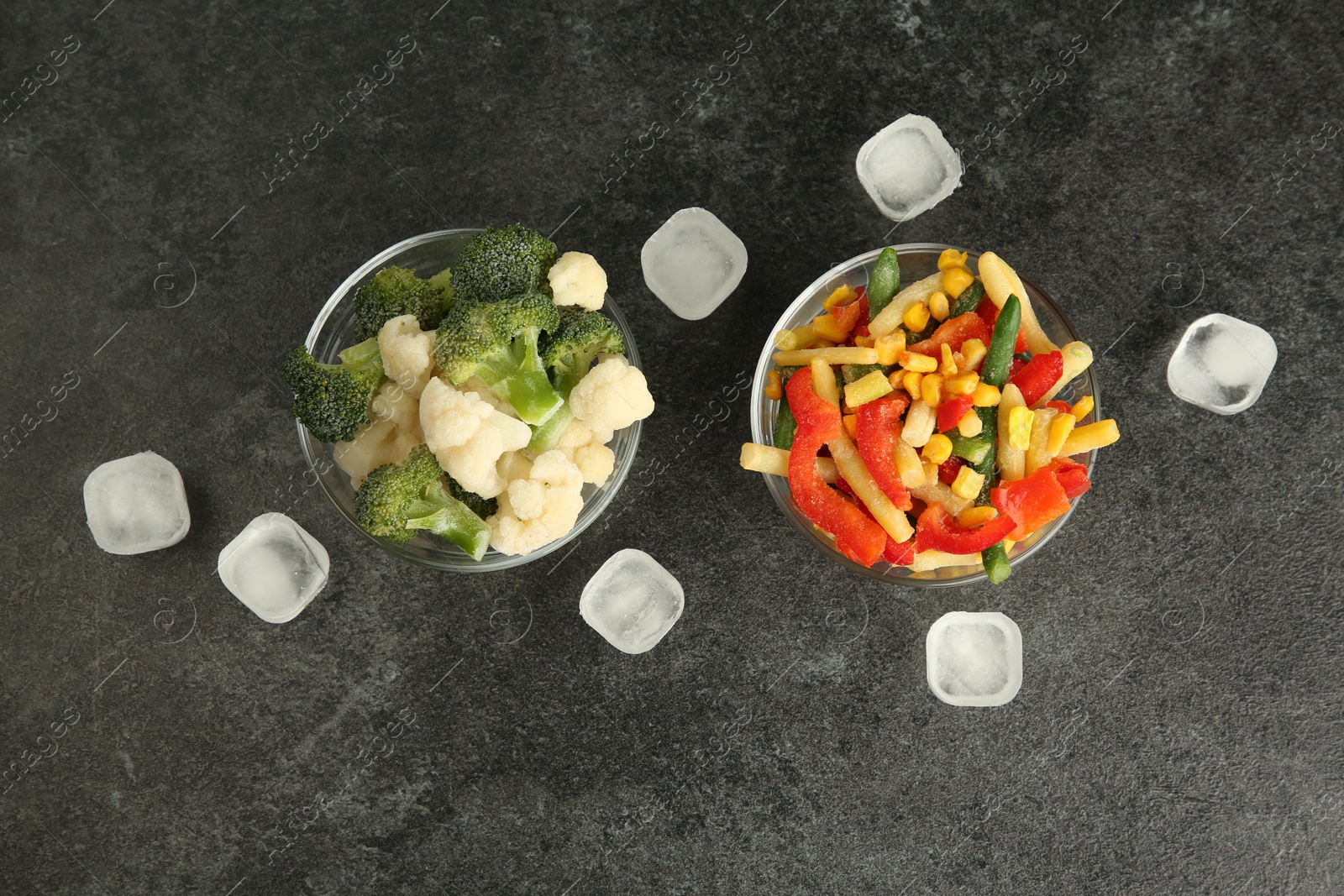 Photo of Bowls of different frozen vegetables and ice cubes on grey table, flat lay