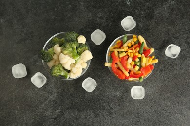 Bowls of different frozen vegetables and ice cubes on grey table, flat lay