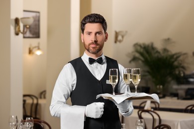 Photo of Butler holding tray with glasses of sparkling wine in restaurant