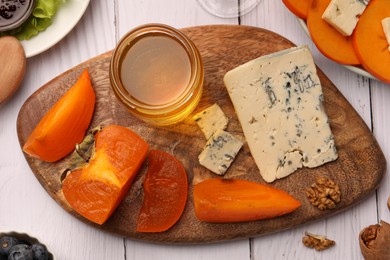 Delicious persimmon with blue cheese on white wooden table, flat lay