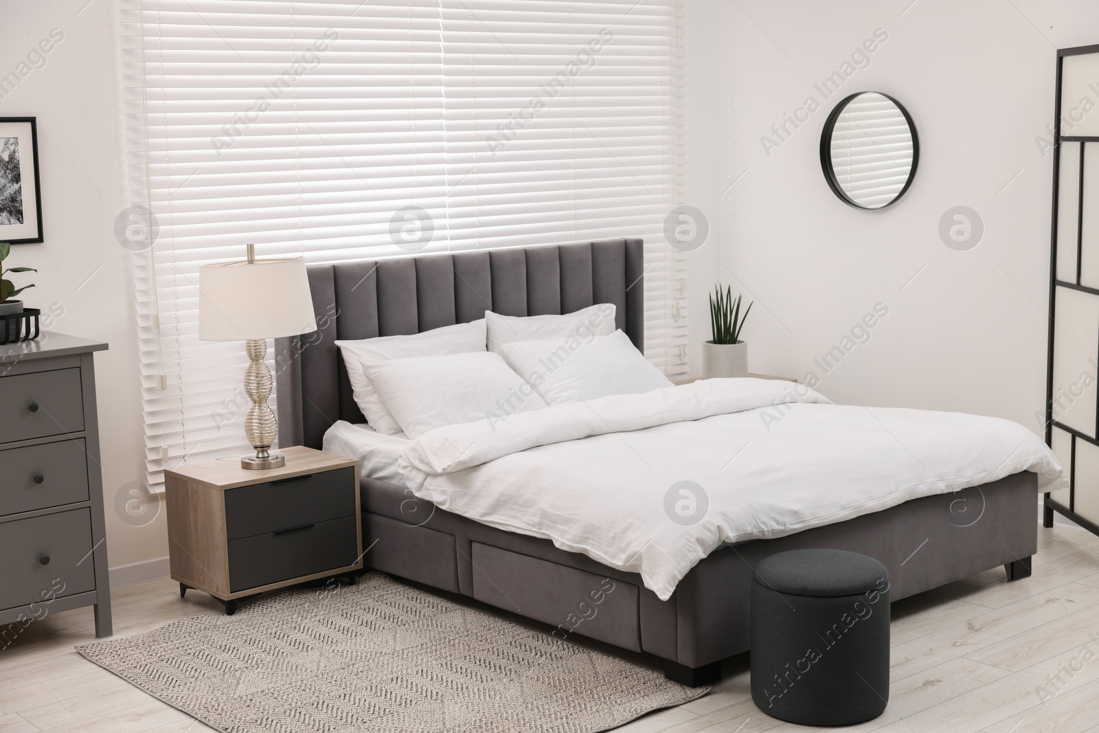 Photo of Stylish bedroom interior with large bed, chest of drawers and lamp