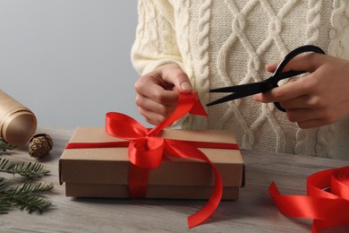 Photo of Woman decorating gift box at wooden table, closeup. Christmas present