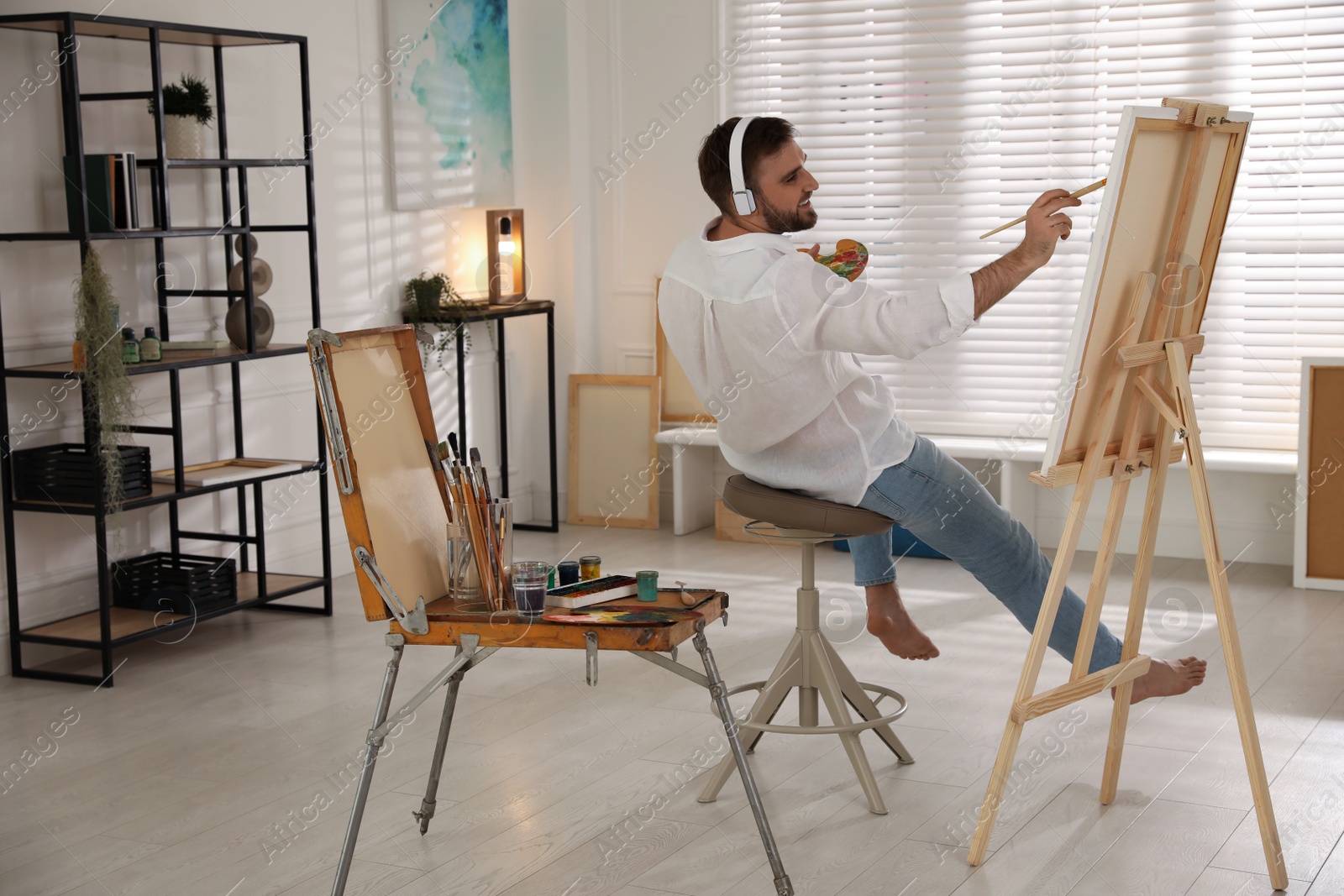 Photo of Young man painting on easel with brush in artist studio