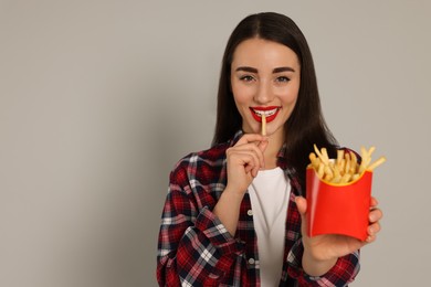 Photo of Beautiful young woman eating French fries on grey background. Space for text