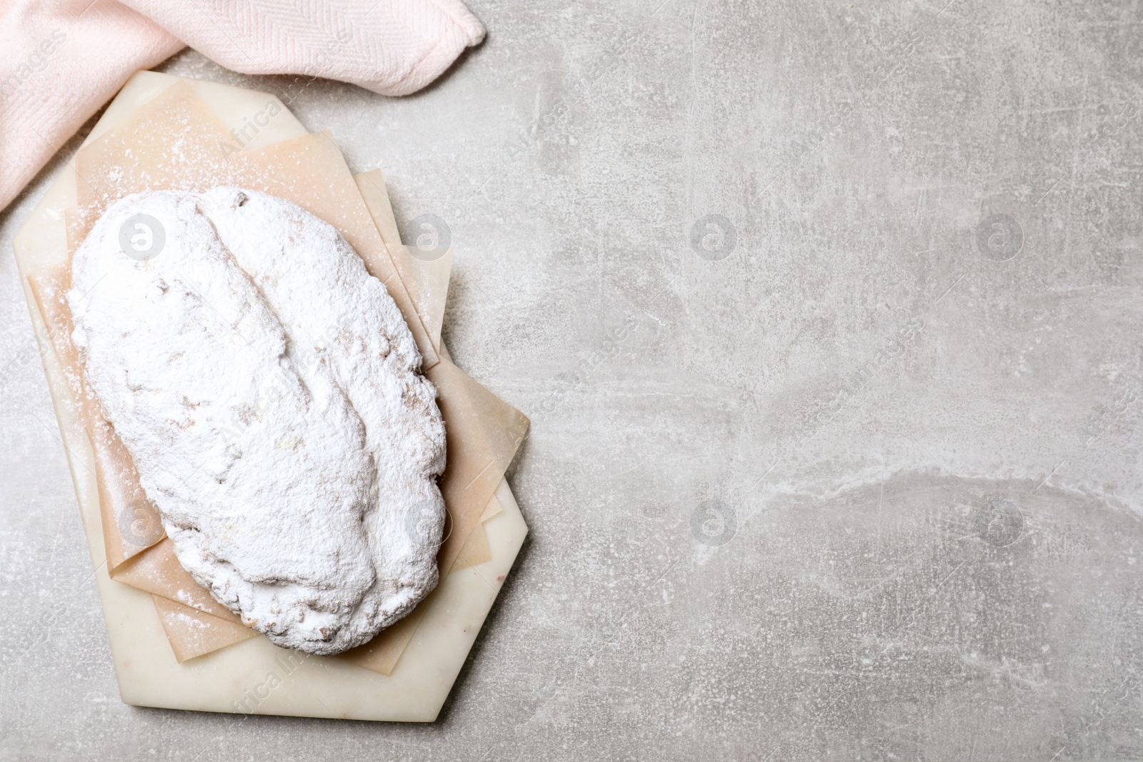 Photo of Delicious Stollen sprinkled with powdered sugar on light table, top view. Space for text