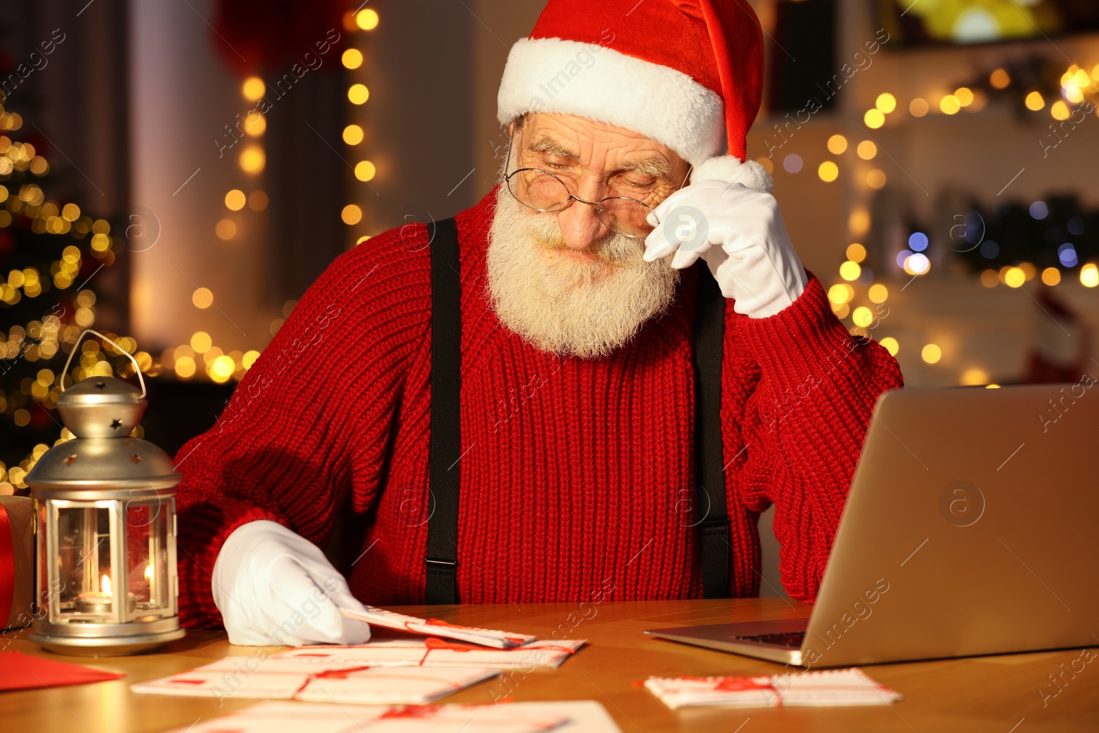 Photo of Santa Claus reading letter at his workplace in room decorated for Christmas