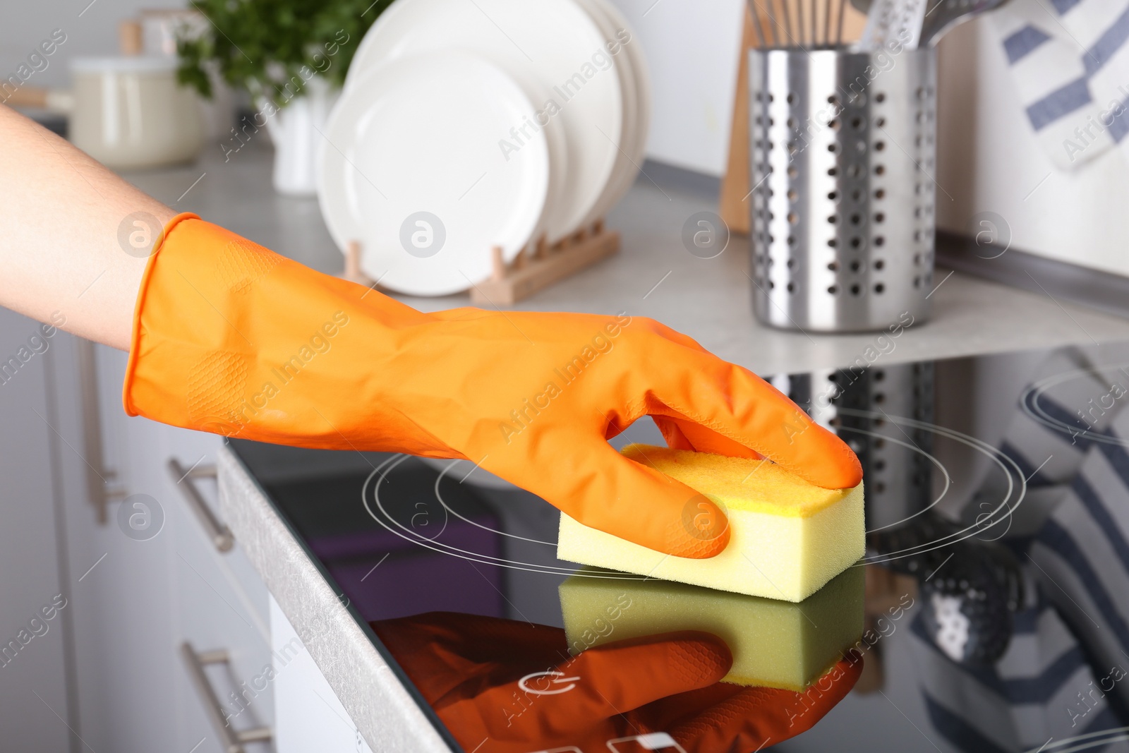 Photo of Woman cleaning oven cooktop with sponge in kitchen, closeup