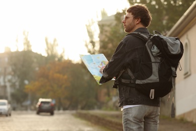 Traveler with world map on city street, back view