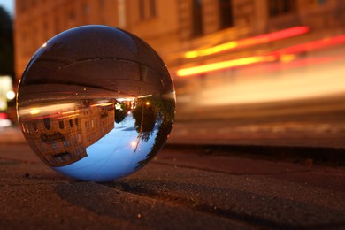Photo of Beautiful city street, overturned reflection. Crystal ball on asphalt road at night. Space for text