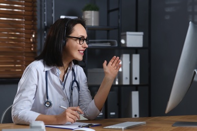 Photo of Doctor with headset and computer consulting patient online in office. Hotline service