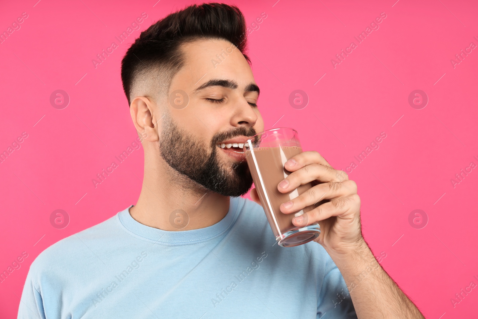 Photo of Young man drinking chocolate milk on pink background