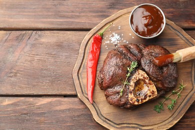 Delicious roasted beef meat served with sauce and spices on wooden table, top view. Space for text