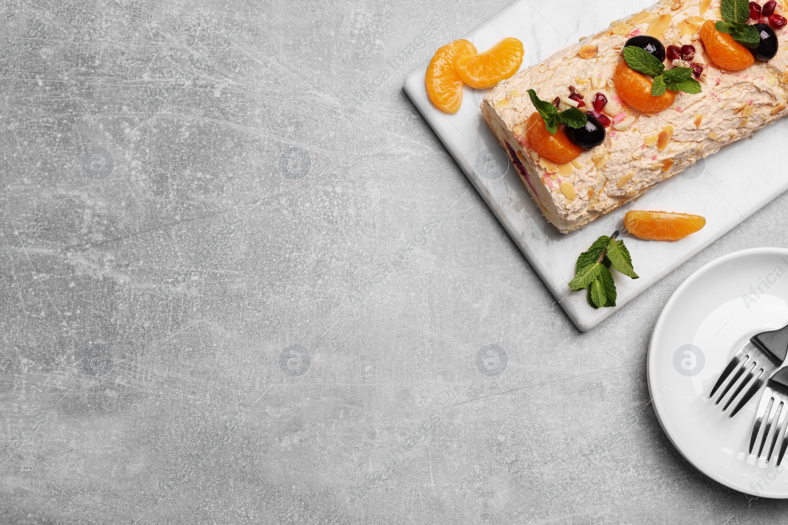 Photo of Tasty meringue roll with tangerine slices and mint leaves on grey table, top view. Space for text