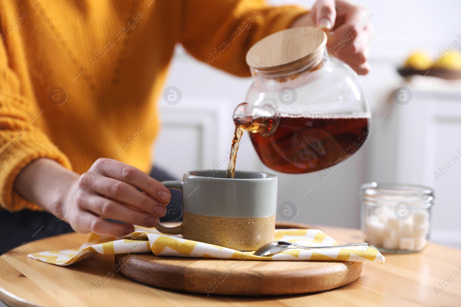 Photo of Woman pouring hot tea into cup at wooden table, closeup