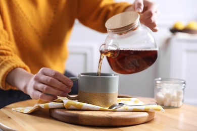 Photo of Woman pouring hot tea into cup at wooden table, closeup