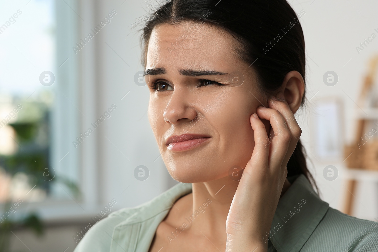 Photo of Young woman suffering from ear pain in room, closeup