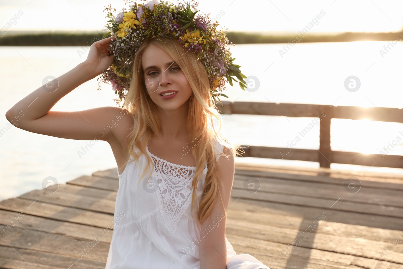 Photo of Young woman wearing wreath made of beautiful flowers on pier near river