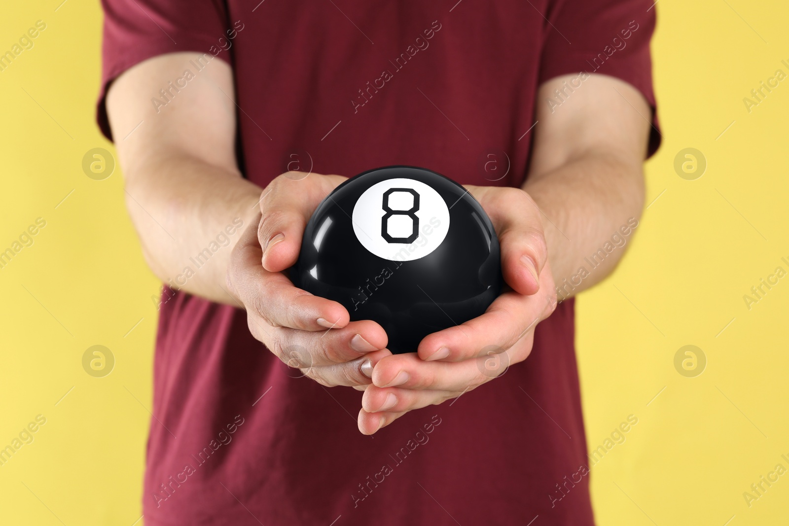 Photo of Man holding magic eight ball on yellow background, closeup