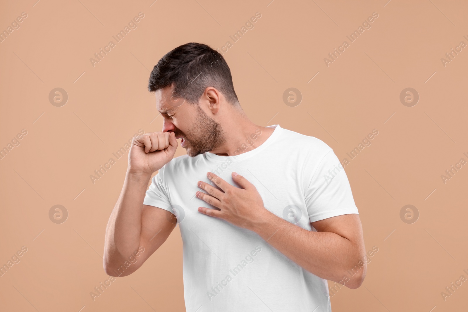 Photo of Allergy symptom. Man sneezing on light brown background