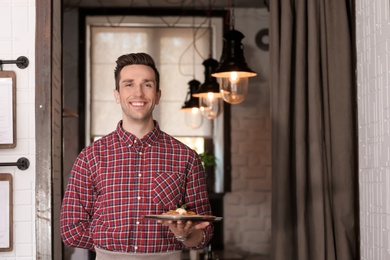 Photo of Young waiter holding tray with tasty dish at workplace