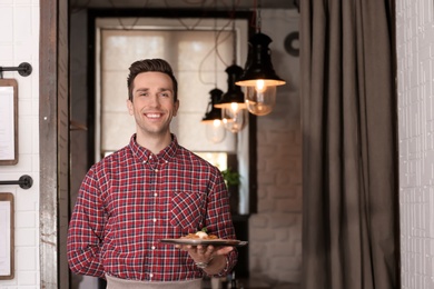 Young waiter holding tray with tasty dish at workplace