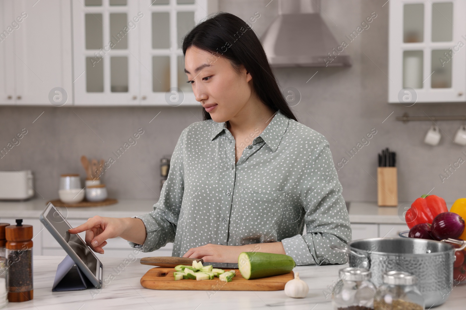 Photo of Beautiful woman searching recipe on tablet while cooking in kitchen