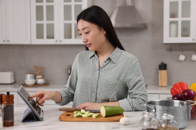 Beautiful woman searching recipe on tablet while cooking in kitchen