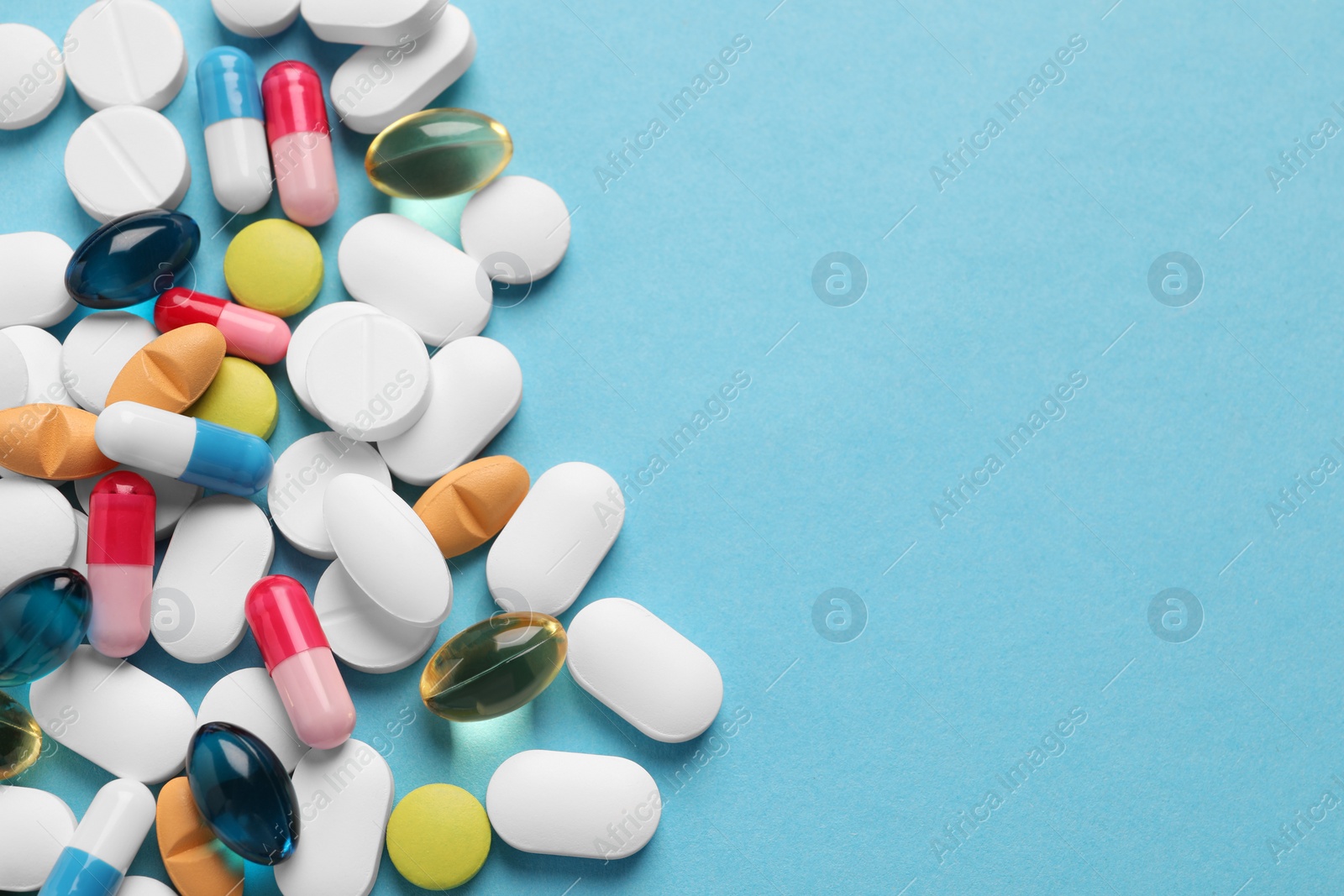 Photo of Pile of different pills on light blue background, flat lay. Space for text