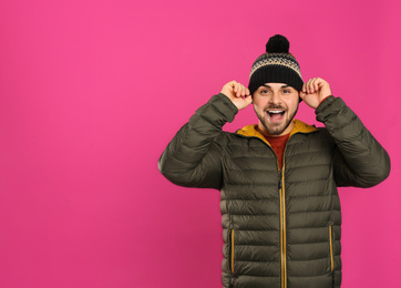 Photo of Happy young man in warm clothes on pink background, space for text. Winter vacation