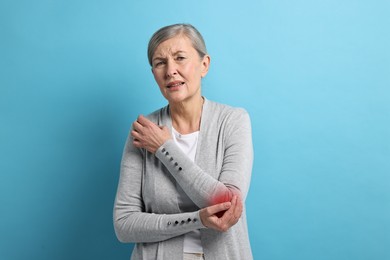 Senior woman suffering from pain in elbow on light blue background