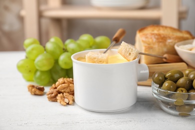 Photo of Pot of tasty cheese fondue and products on white wooden table