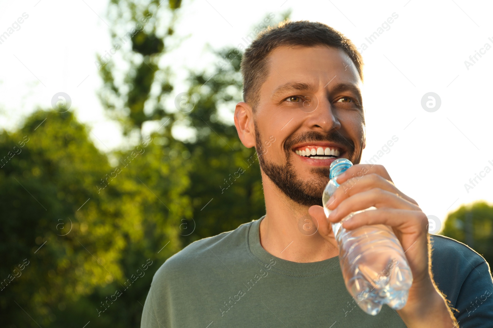 Photo of Happy man drinking water outdoors on hot summer day. Refreshing drink