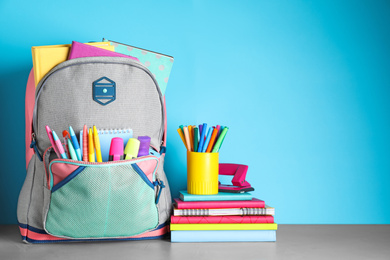 Stylish backpack with different school stationery on table against light blue background. Space for text