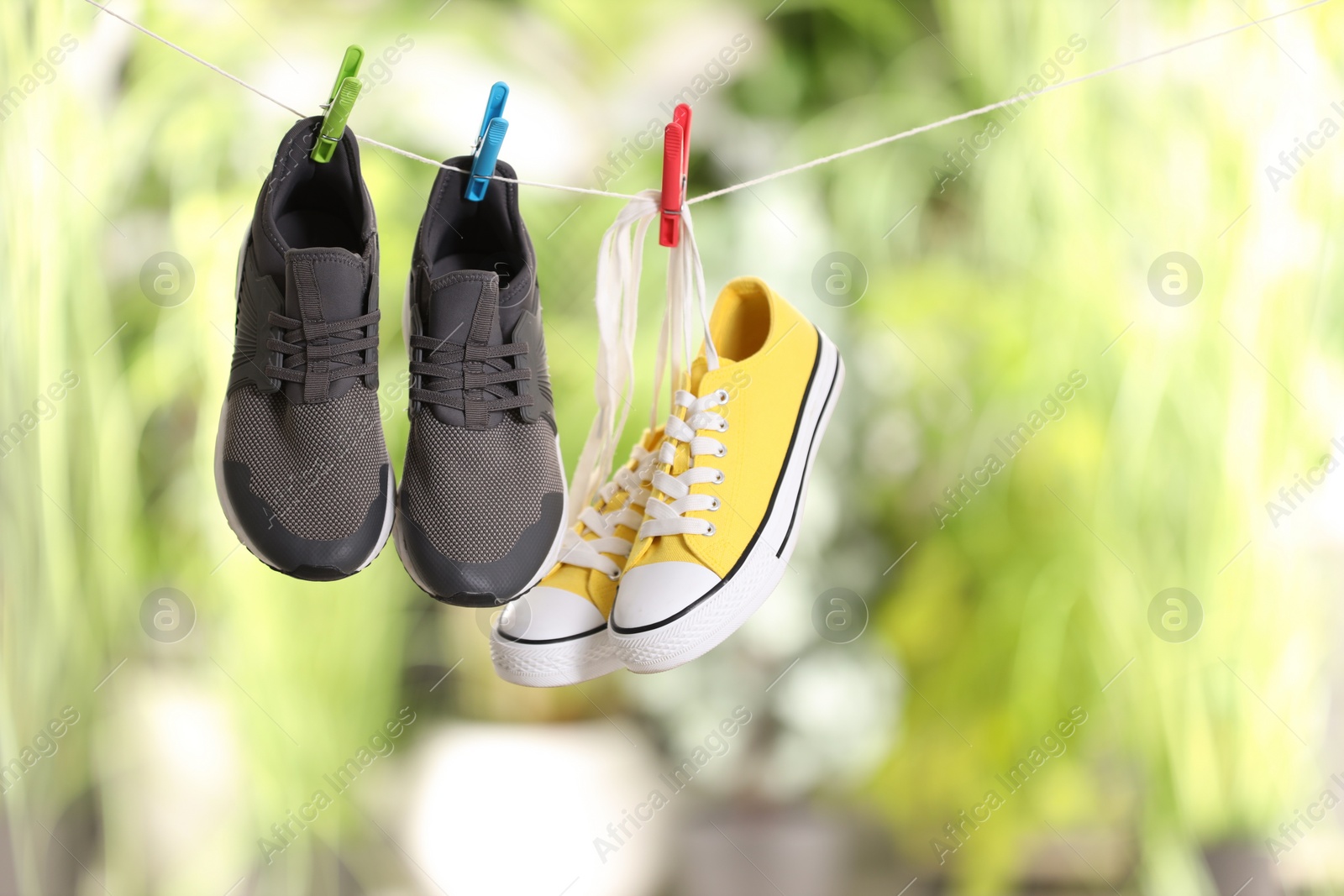 Photo of Different stylish sneakers drying on washing line against blurred background