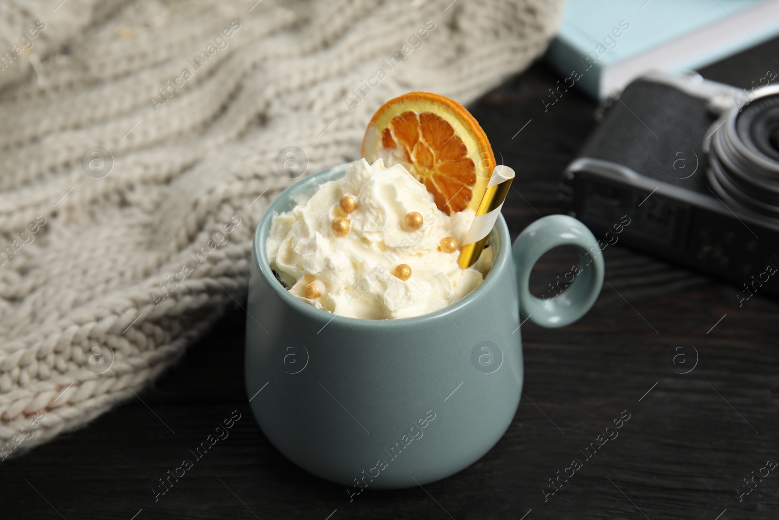 Photo of Cup of hot winter drink with whipped cream and knitted scarf on black wooden table