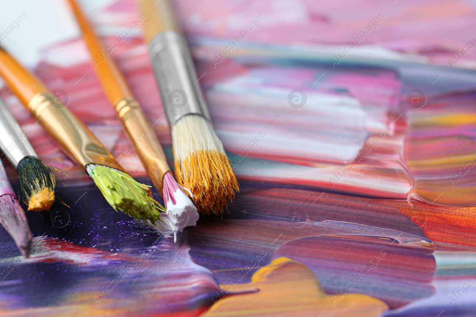 Photo of Set of different brushes on abstract colorful paint, closeup