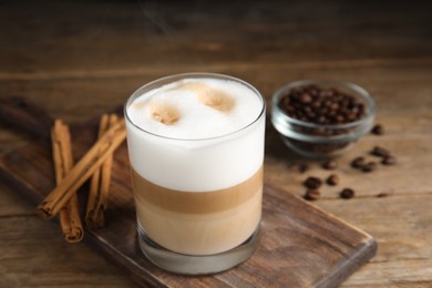 Photo of Delicious latte macchiato, cinnamon sticks and coffee beans on wooden table