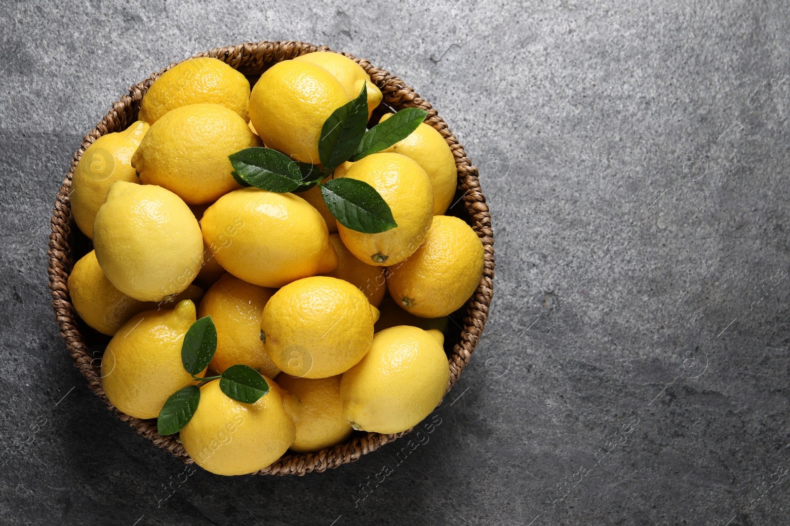 Photo of Fresh lemons in wicker basket on grey table, top view. Space for text