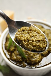 Photo of Spoon of tasty arugula pesto near bowl with sauce, closeup