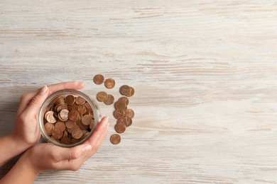 Woman holding glass jar with coins on white wooden table, closeup. Space for text