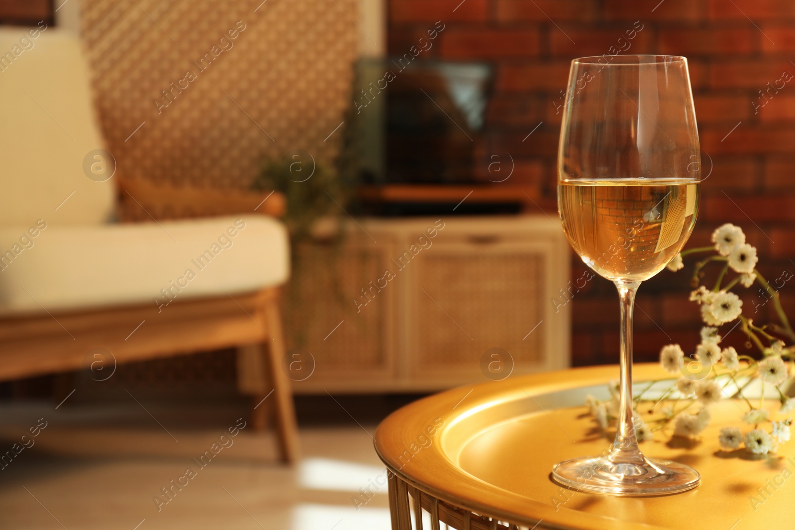Photo of Glass of white wine and flowers on table in room, space for text. Relax at home